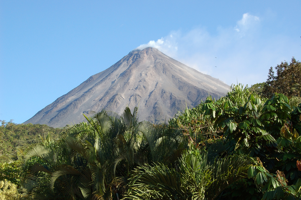 The smoking cone of Mount Arenal is visible on a perfectly clear day rising above lush jungle vegetation.