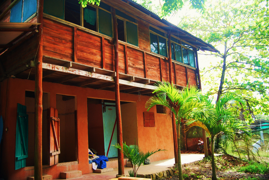 View of a two story wooden house with a porch running around the second floor.