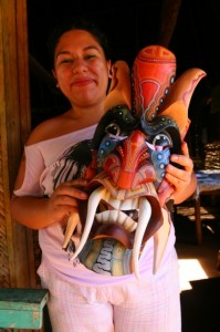 A Boruca craftswoman holds up a colorful carved mask with large tusklike teeth.