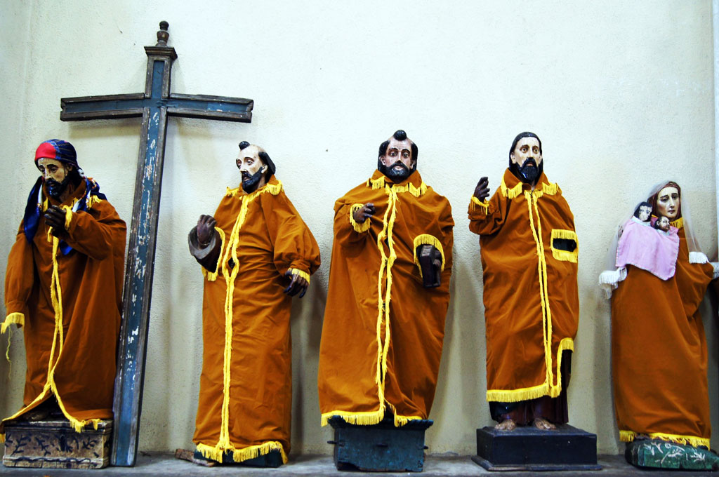 A wooden cross and figurines of saints in orange robes propped against a wall.