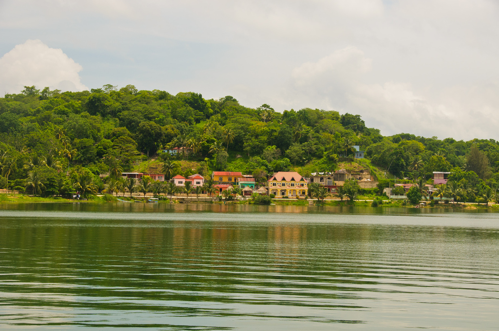 View of colorful houses clustered on a verdant shore across a calmly rippling lake.