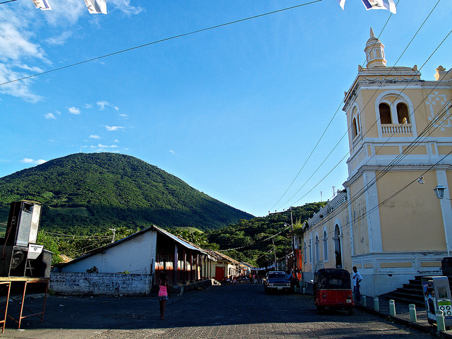 A verdant volcanic peak rises behind a yellow colonial church trimmed in white.