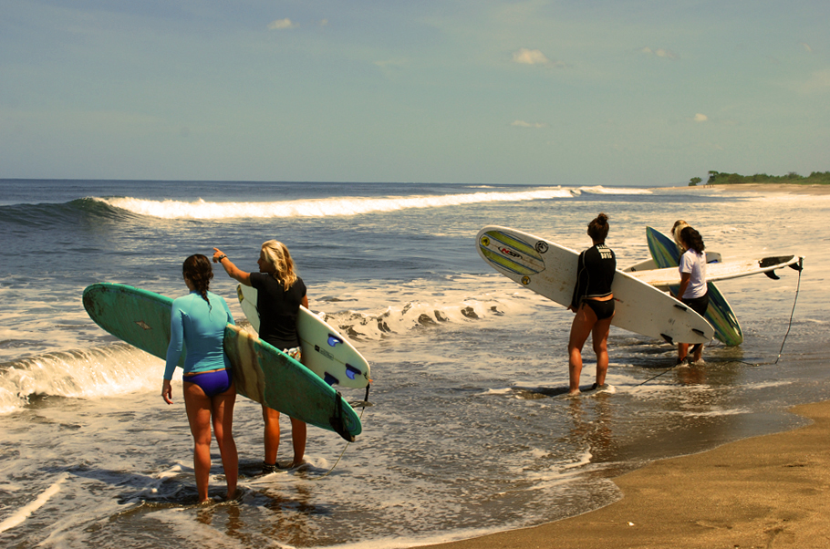 Four women surfers stand at the edge of the water in Nicaragua.