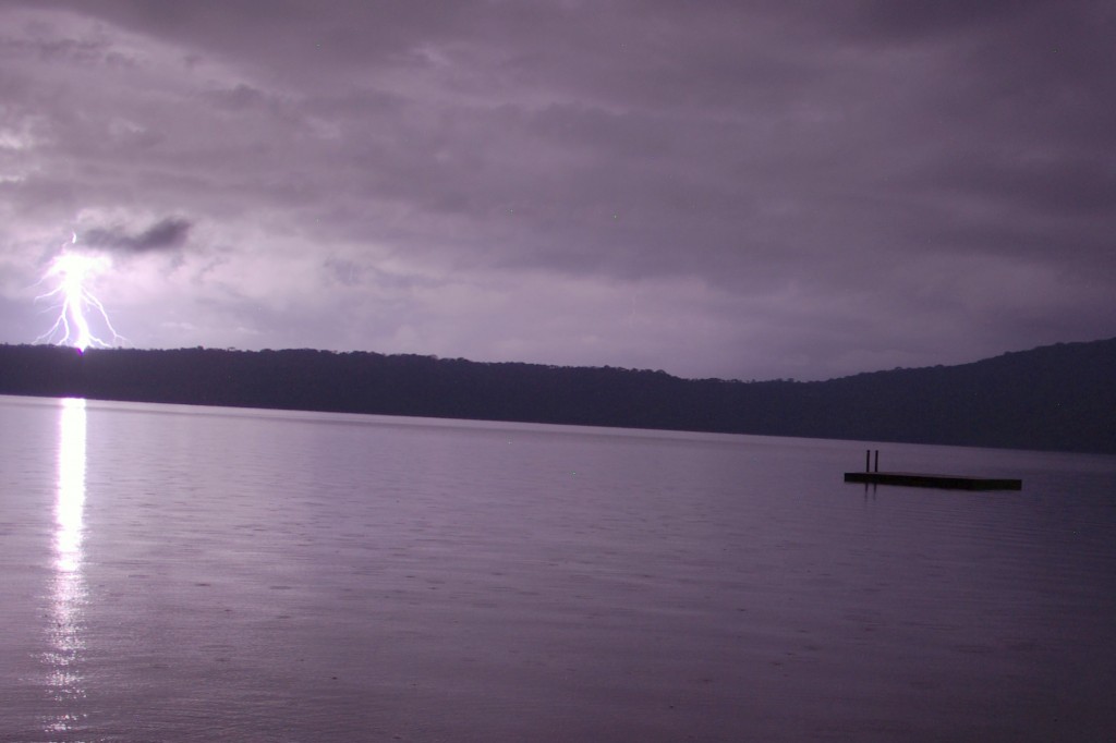 Lightning strikes far in the distance beyond the flat calm waters of the lake.