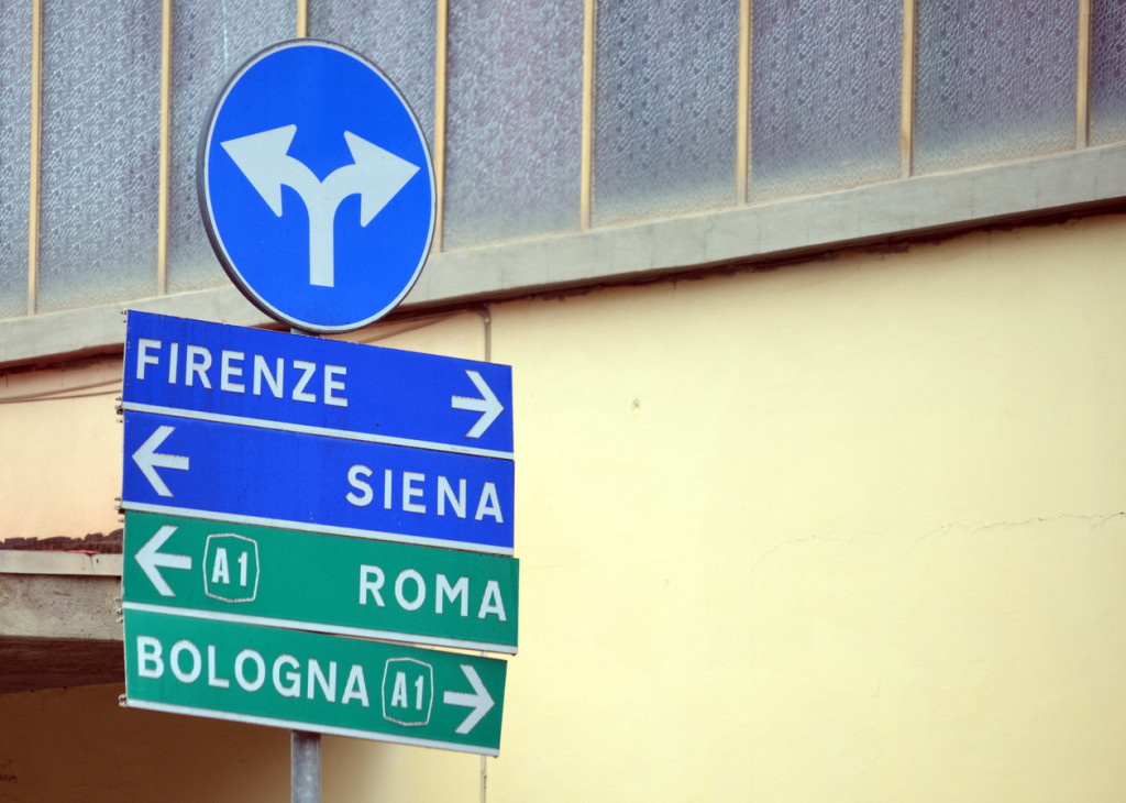 A round sign with split arrows is at the top of a row of signs listing cities and accompanied by left and right arrows.