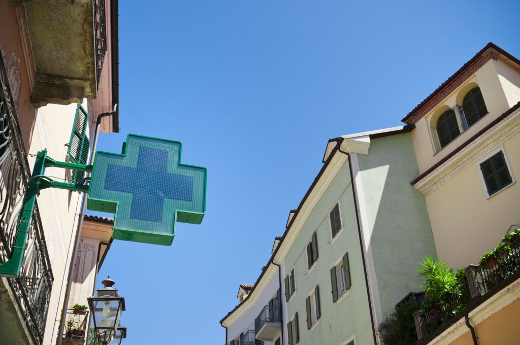 A sign in the shape of a blue cross hangs on the side of a building indicating a pharmacy.