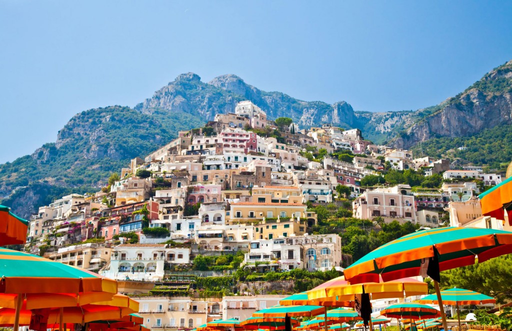 Colorful, multistoried buildings cluster tightly on a hillside overlooking bright beach umbrellas.