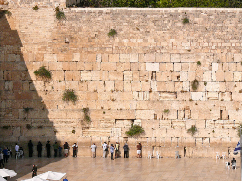 Visitors line up against the high stone wall in prayer.
