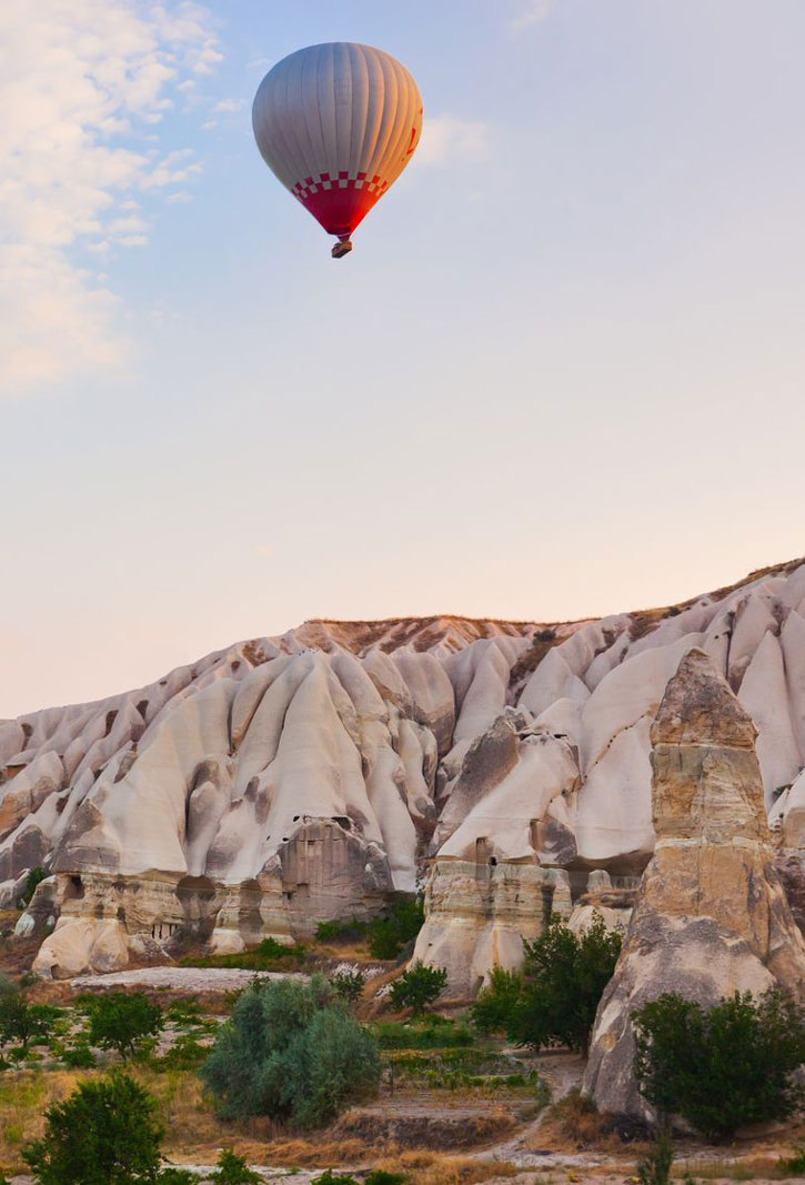 A single hot air balloon floats over the Cappadocia landscape.