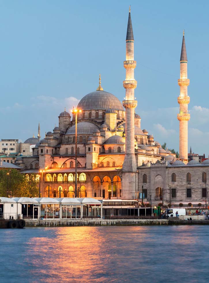 Golden lights from the Yeni Cami mosque reflect off the waterfront at dusk.