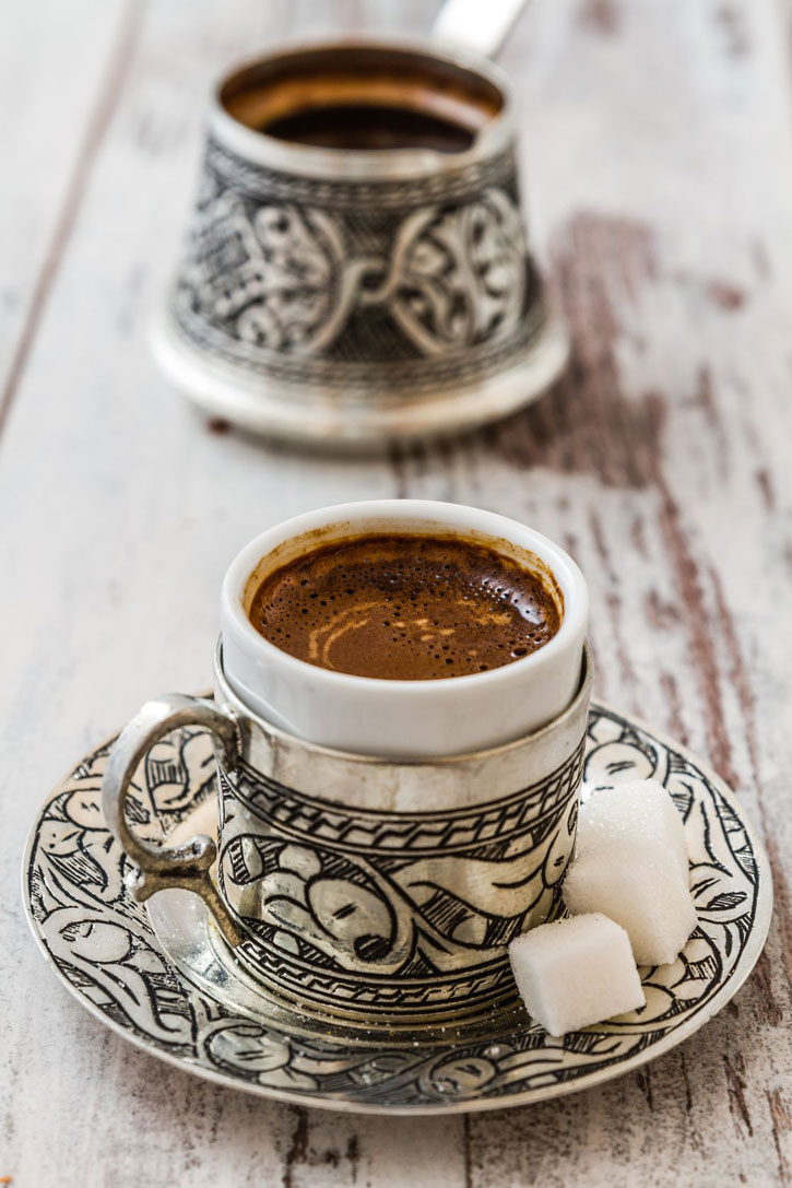 Turkish coffee in a traditional silver demitasse cup and matching pot.