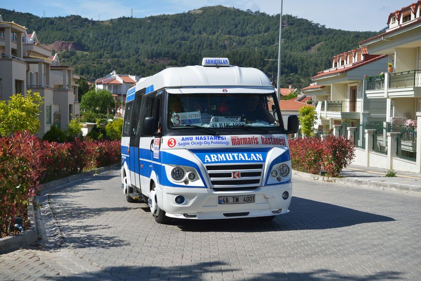 A white and blue dolmuş or minibus travels through Marmaris, Turkey.
