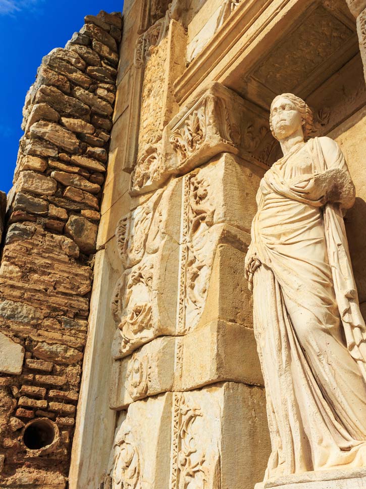 A statue set in an alcove with intricate carvings in the ruins of Ephesus.