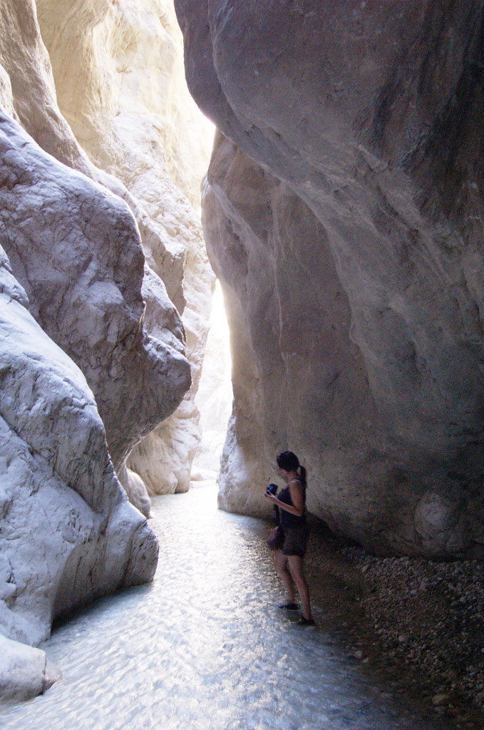 A woman stands near water flowing between a passage through narrow white rock walls in Turkey's Saklikent Gorge.