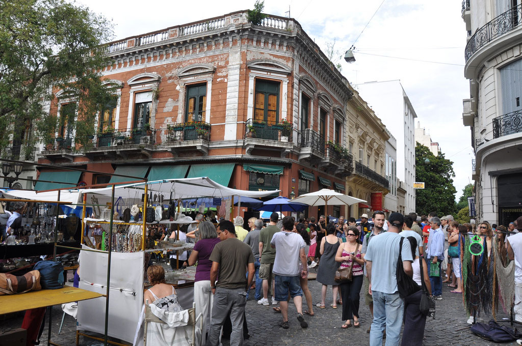 With colonial buildings on the corner of the block, pedestrians crowd the street between tent stalls.