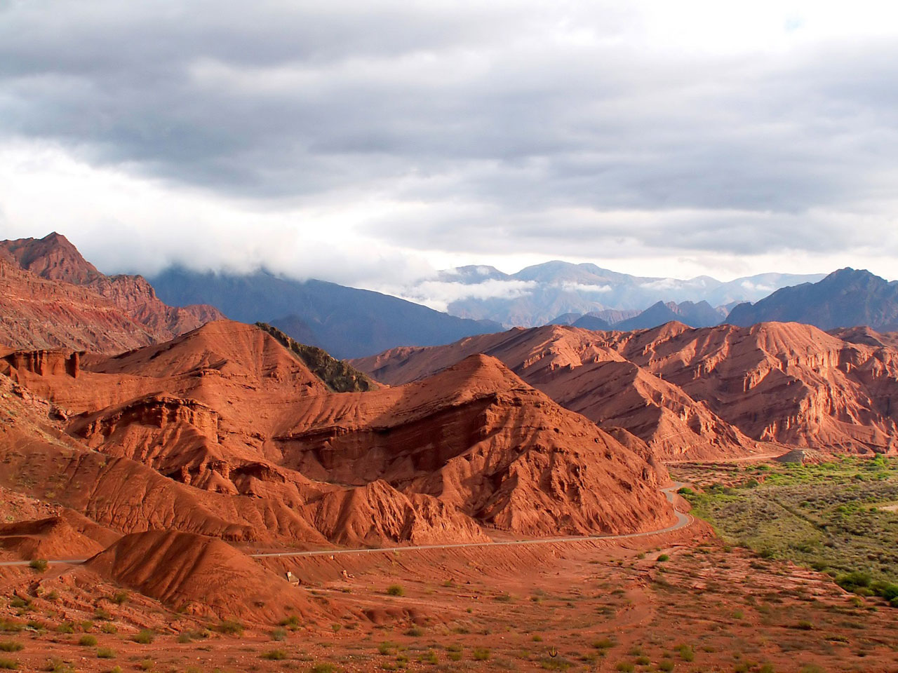 Grassland abuts red stone mountains with snow-covered mountains off in the distance.