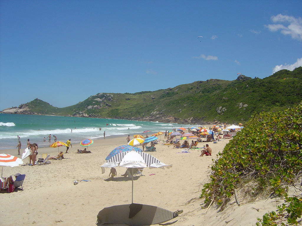 A beautiful sandy beach on curving coastline with visitors scattered amongst colorful umbrellas.