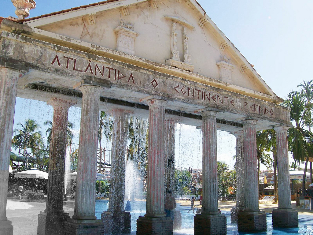 A greek temple-facade stands next to a pool fountaining water.