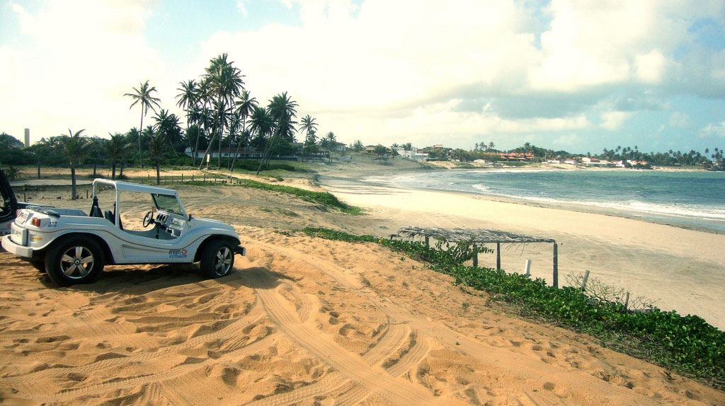 A dune buggy is parked on golden sand as waves roll in gently onto the shore.