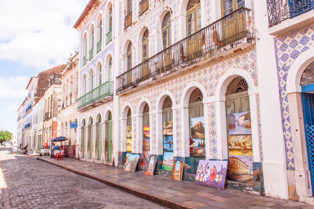 View down a row of colonial buildings with painting lined up on the sidewalk.