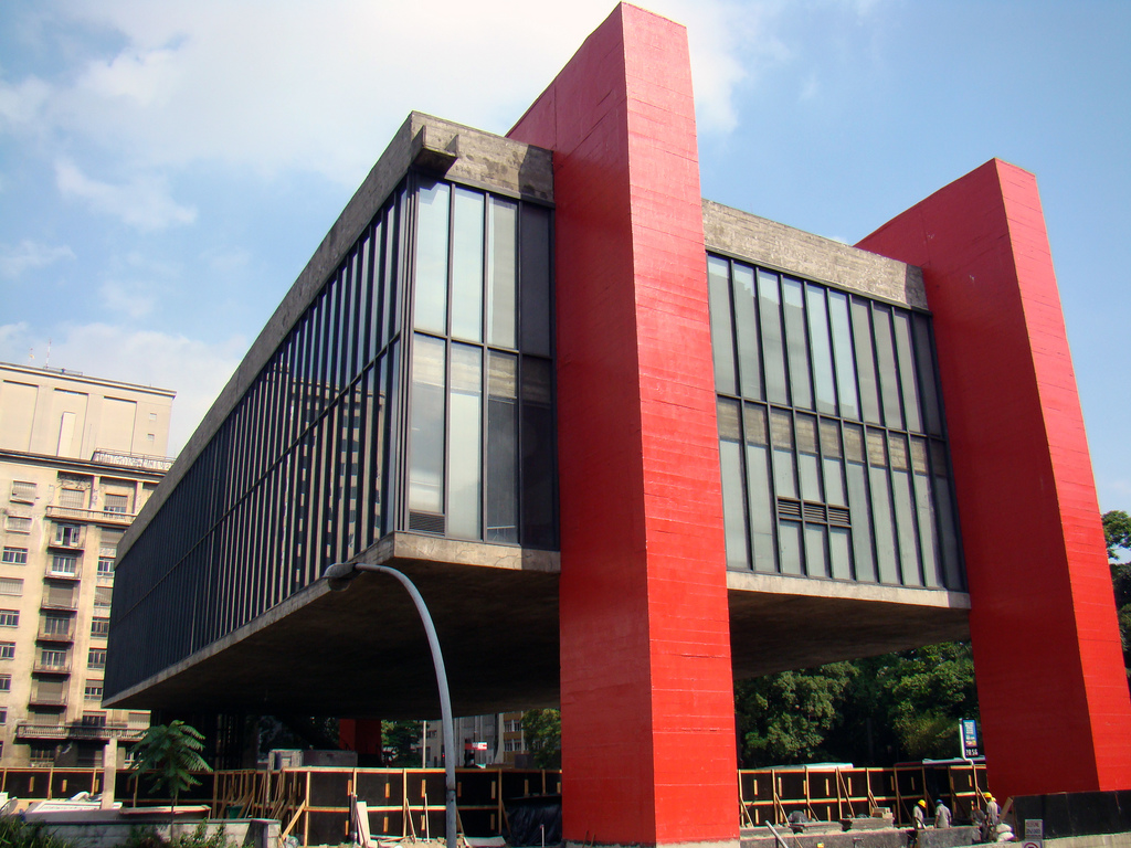 A modern glass-faced building with dramatic red support elements.