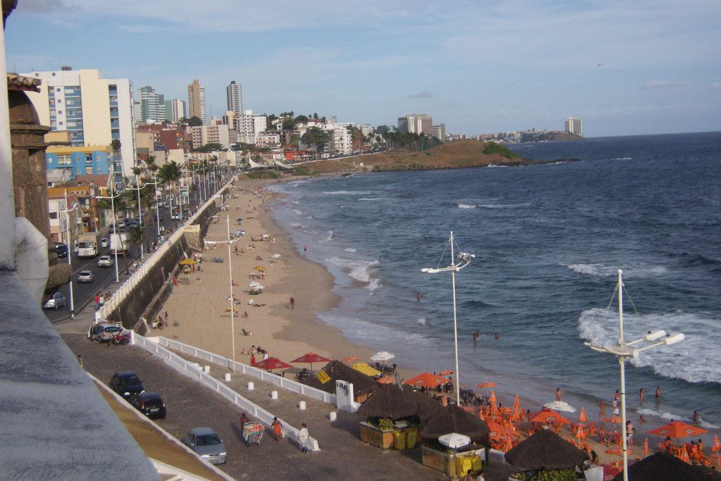 Balcony view down to a narrow beach butting up against a long coastal road.