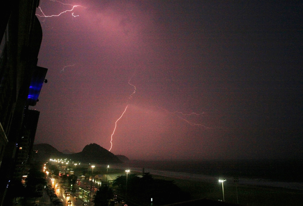 Lightning illuminates the sky at night over a view of cars lining the road.