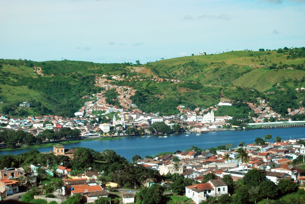 Colonial buildings, many of them white with terra cotta roofs, cluster on either side of a narrow blue river.