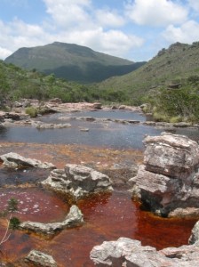 Water pools around rocks that are red with minerals in a small river.