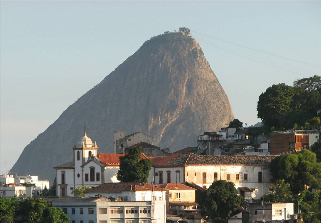 View of multi-story white-washed buildings built into the hillside with Sugarloaf Mountain visible beyond the rooftops.