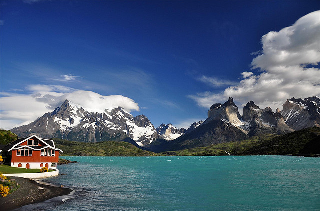 A red hotel with white trim sits on the shores of Lago Pehoé with the park's dramatic peaks visible across the water.