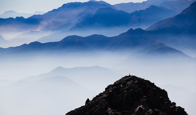 Blue misty mountain peaks fading into the distance with a mountain peak in the foreground.