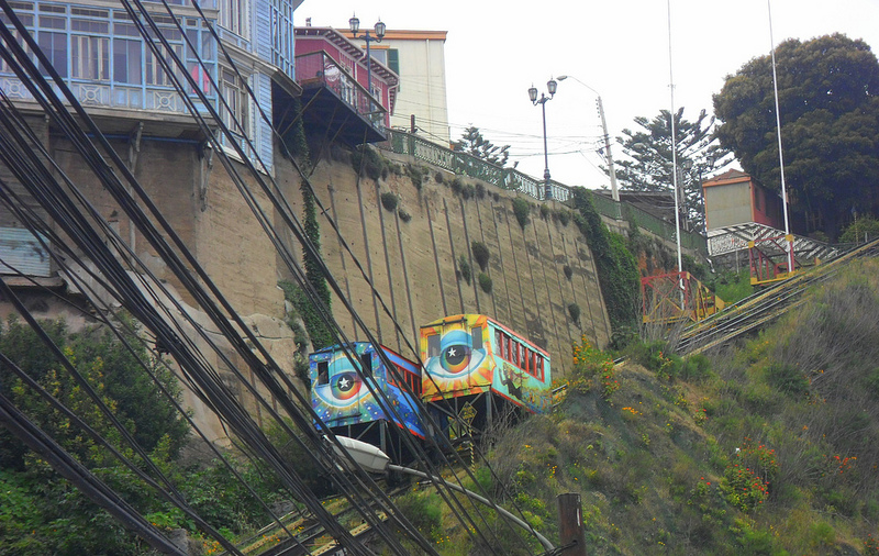 Two funiculars painted with colorful graffiti-style pop artwork move along the hillside.