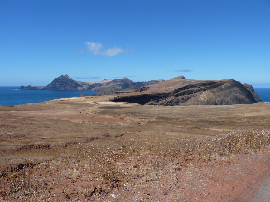 View across a narrow, flat expanse surrounded by ocean with another smaller island visible in the distance.