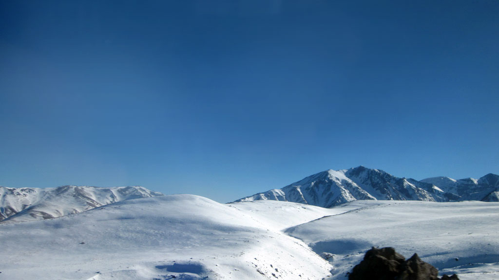 View across a snowy slope with a mountain range visible in the distance.