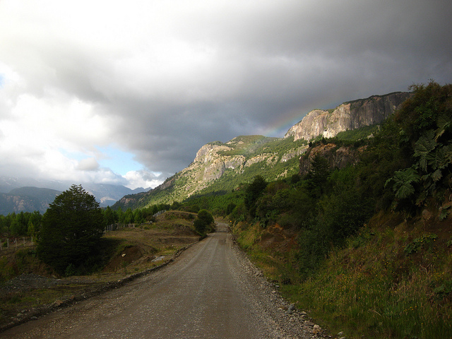 A packed gravel road cuts through green hillsides with exposed rock walls.