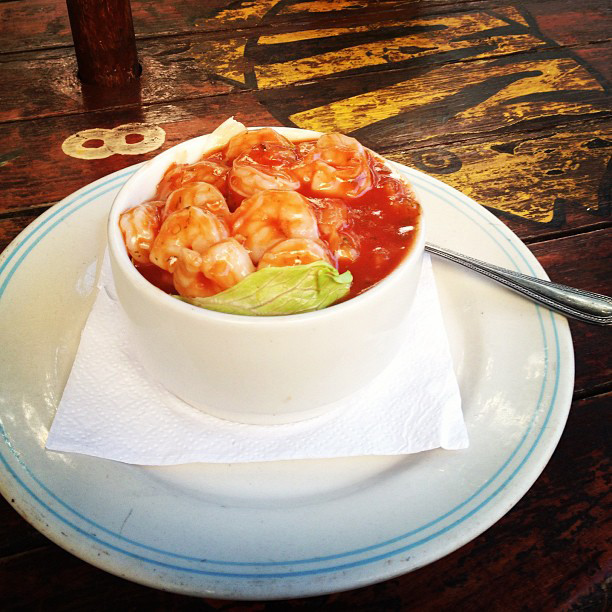 A small bowl of shrimp ceviche sits on a wooden table.
