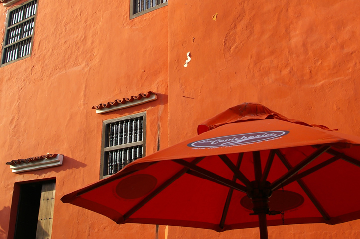 An orange umbrella shades a table in front of an orange wall at La Cevichería.