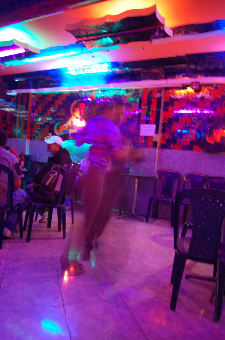 A couple dances a salsa in a neon-lit bar.