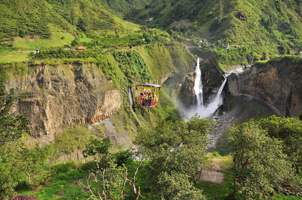 A suspension trolley crosses high above a valley with a heavily flowing waterfall.