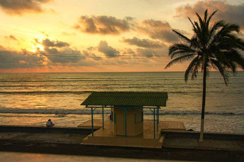 A small structure silhouetted on the shore at sunset.