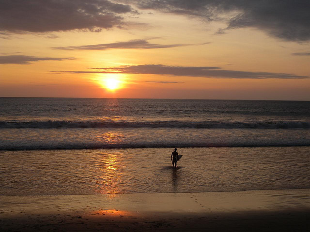 A surfer carrying his board into the water is silhouetted.