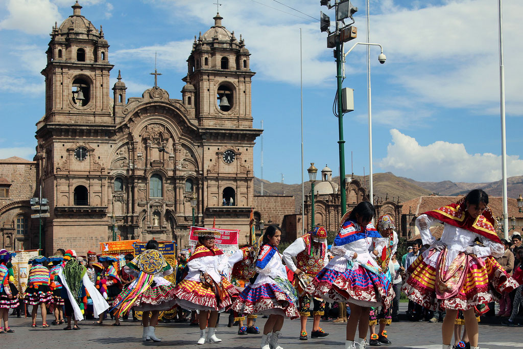 Women in colorful traditional dresses dance in in the plaza.