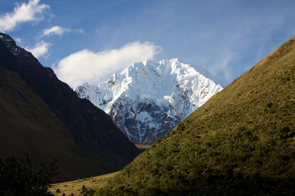 View of a snow-capped mountain visible through a steep valley between two verdant hillsides.