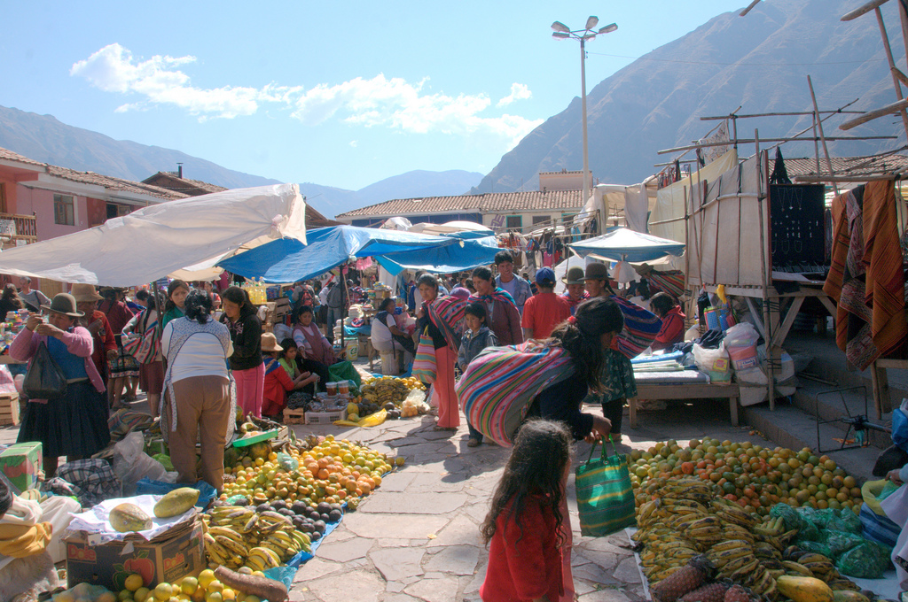 Fruits and other wares are displayed in a busy street market.