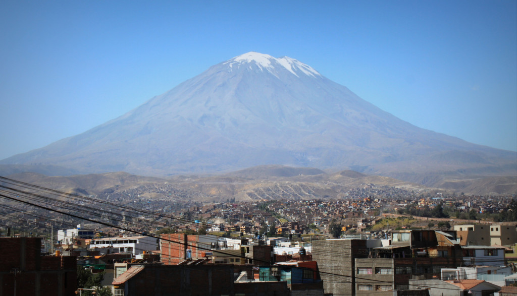 View across the Yanahuara district of Arequipa with a massive, snow-capped volcano dominating the sky in the distance.