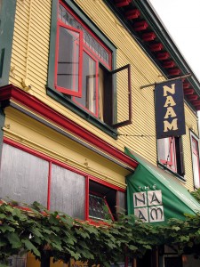 Ivy grows along the front of a yellow building with red trim and a green overhang that reads NAAM.