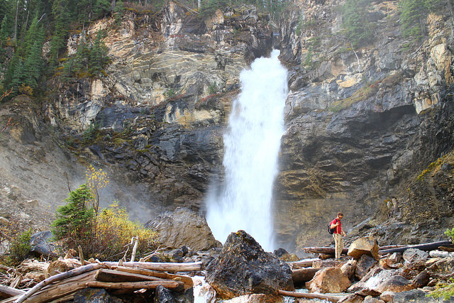 A hiker crosses a log and boulder-strewn stream in front of Laughing Falls in Yoho National Park.