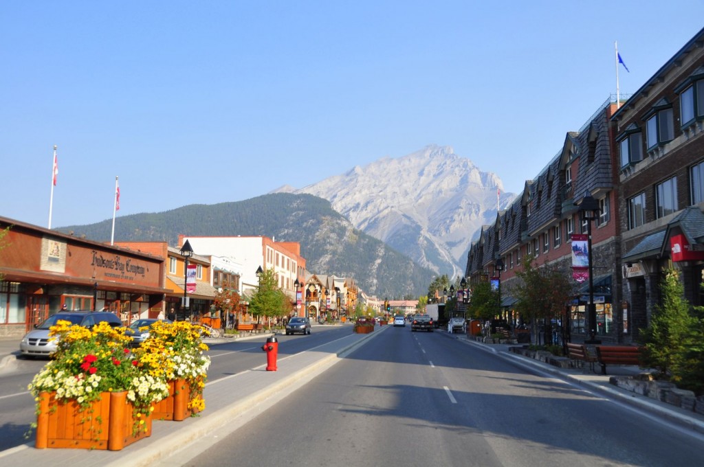 A quaint looking town with brick buildings and flower boxes on the street and the dramatic snow-covered rise of mountains in the distance.