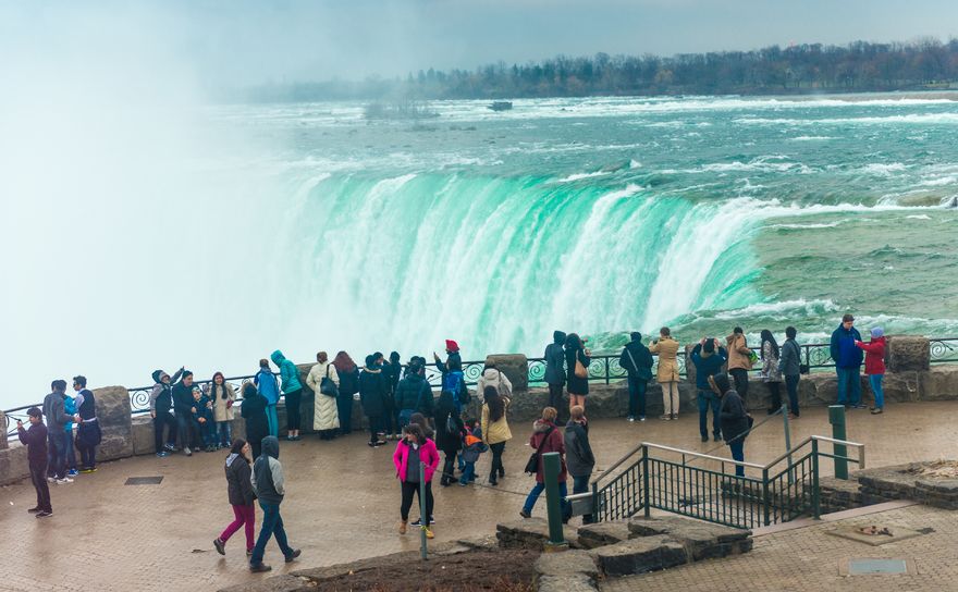 Pedestrians line up against a rail to watch the falls spill over on the Canadian side of Niagara Falls.